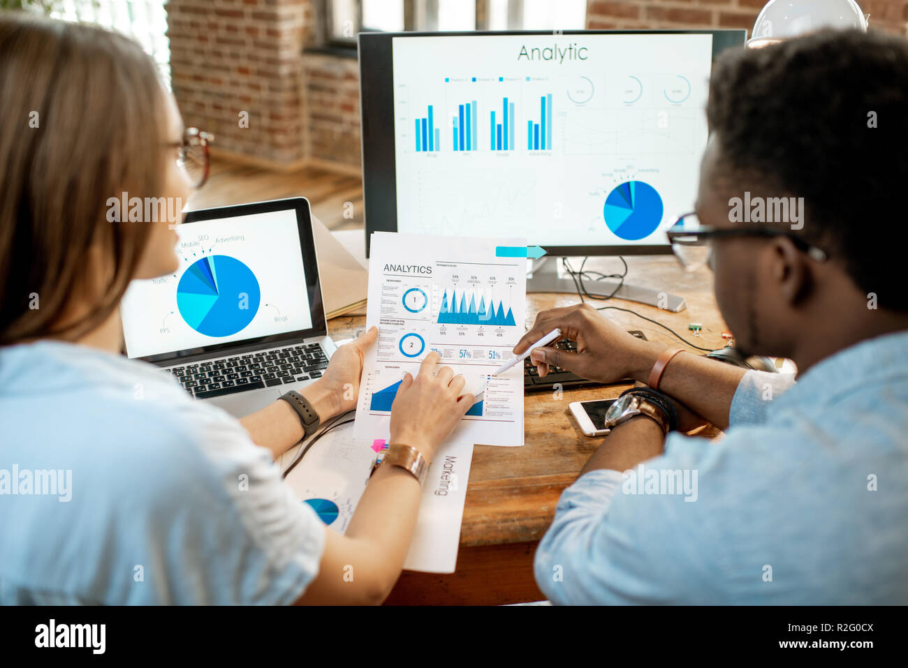 I collaboratori di lavorare con analitycs seduti insieme al posto di lavoro con computer, laptop e documenti. Vista da dietro incentrate sui documenti Foto Stock