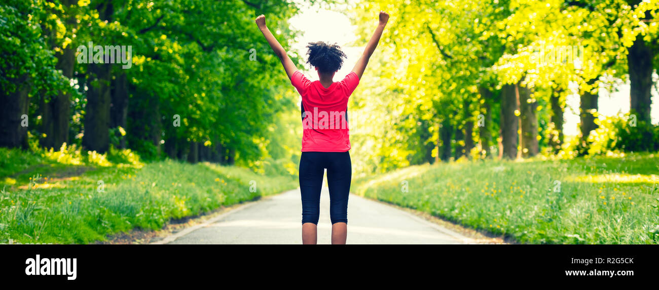 Panoramica banner web splendida razza mista americano africano donna giovane ragazza adolescente fitness jogging in esecuzione per celebrare il successo sulla strada fiancheggiata con sp Foto Stock