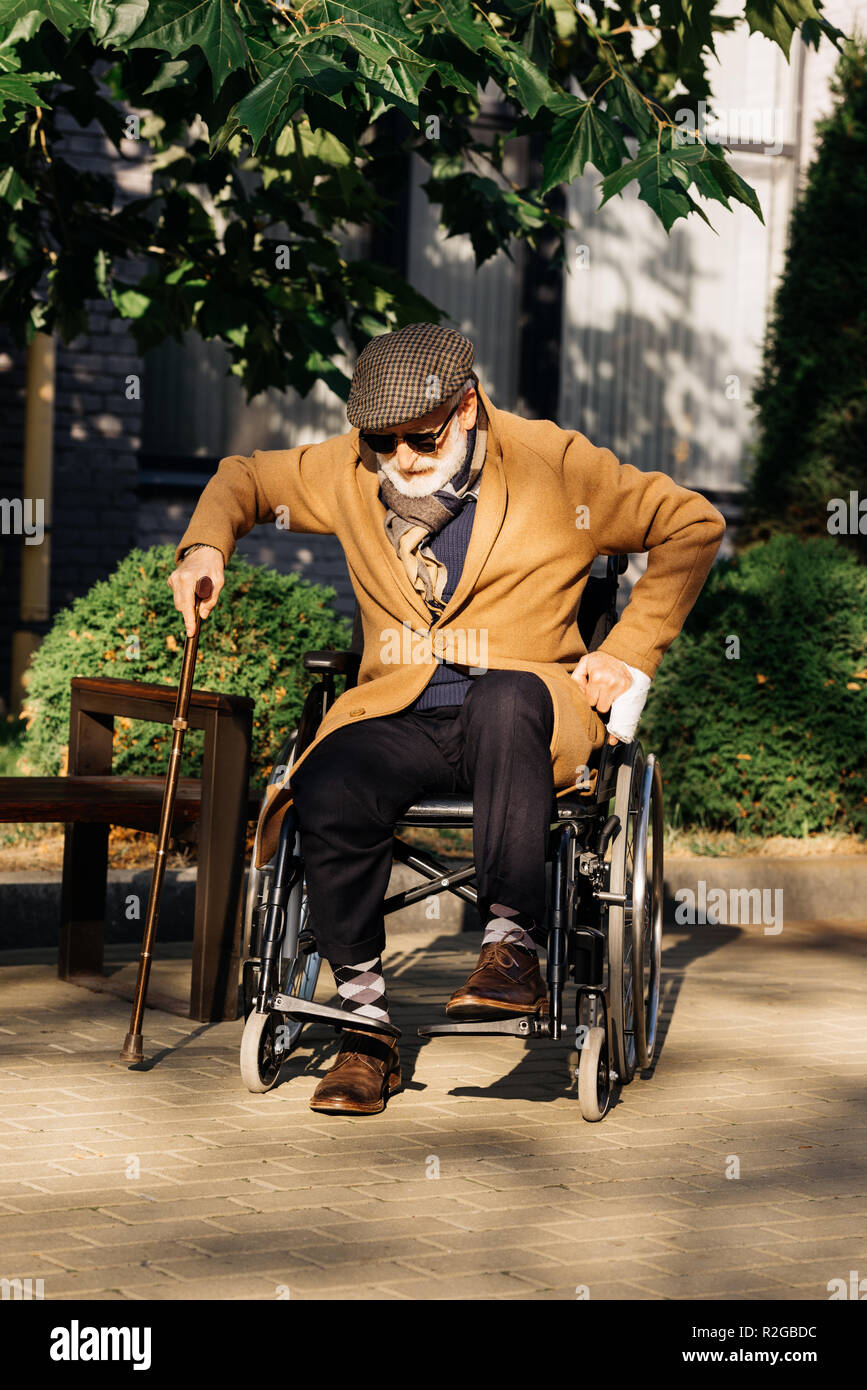 Senior uomo disabili cercando di alzarsi dalla sedia a rotelle con bastone  su strada Foto stock - Alamy