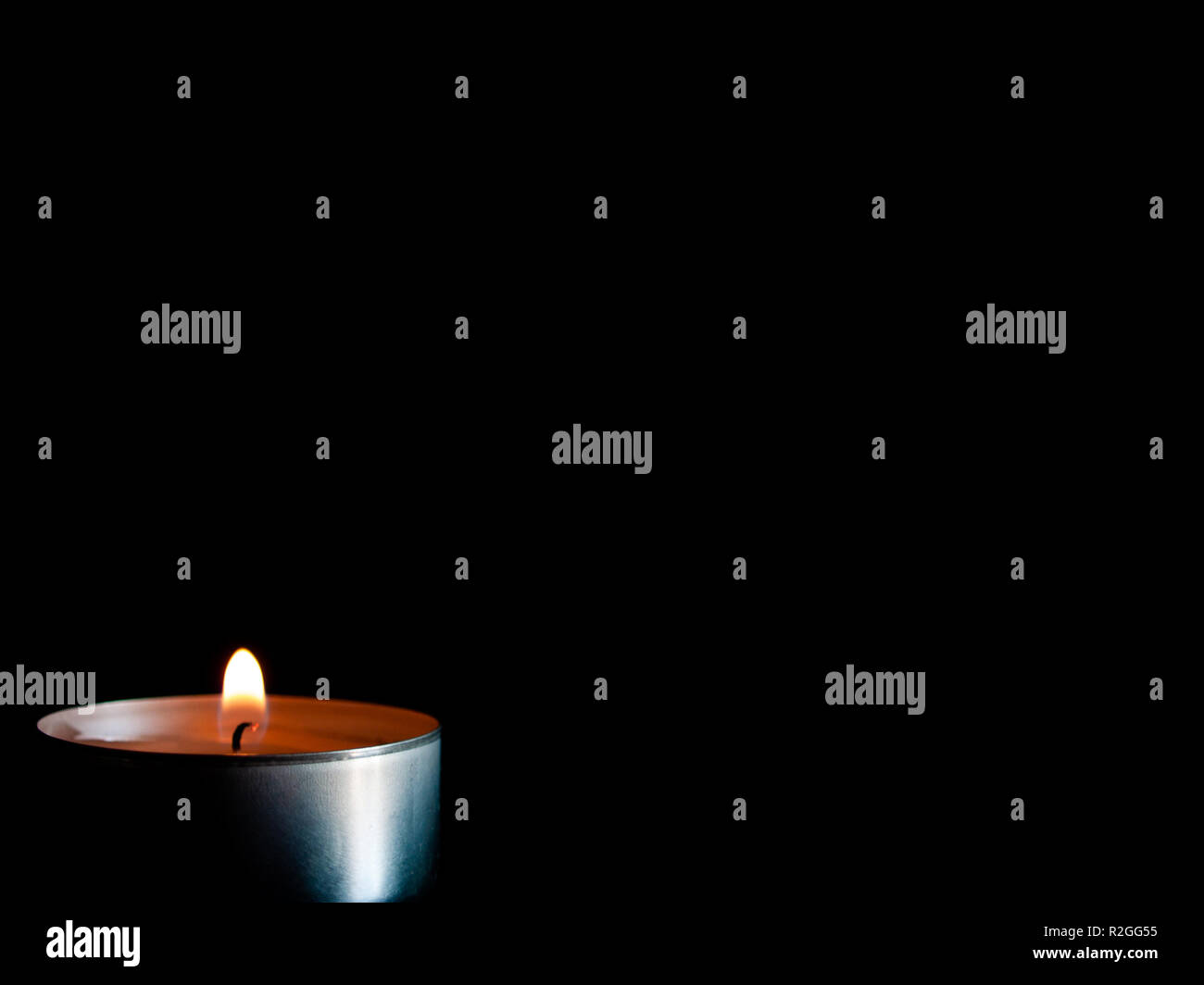 Una candela accesa con una fiamma di colore arancione e isolate su uno sfondo nero Foto Stock