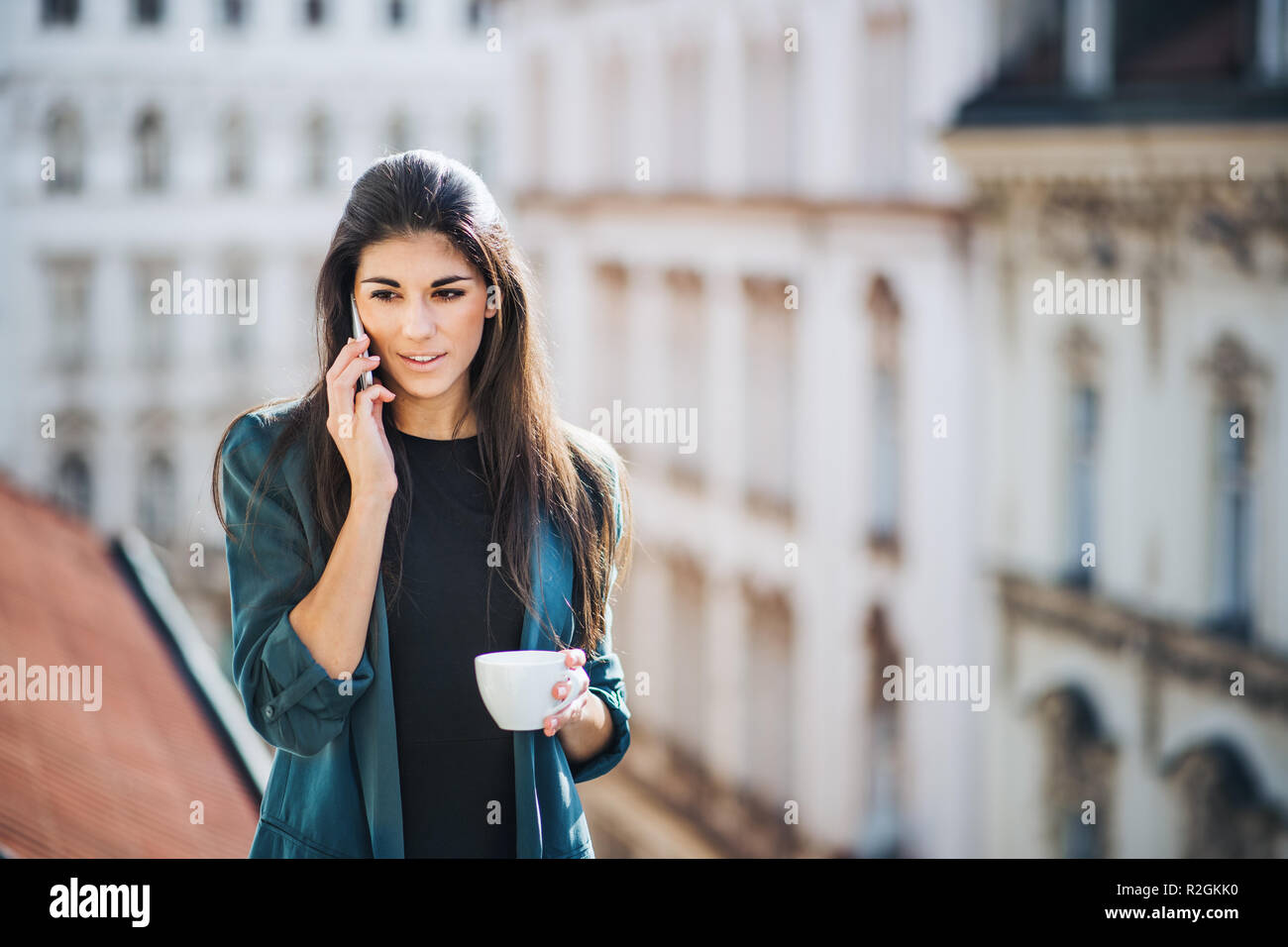 Giovane imprenditrice con lo smartphone in piedi su una terrazza al di fuori di un ufficio in città. Foto Stock