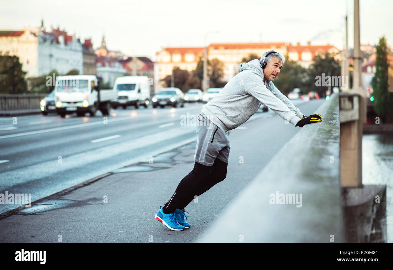 Maschio maturo runner con cuffie stretching all'aperto sul ponte nella città di Praga. Foto Stock