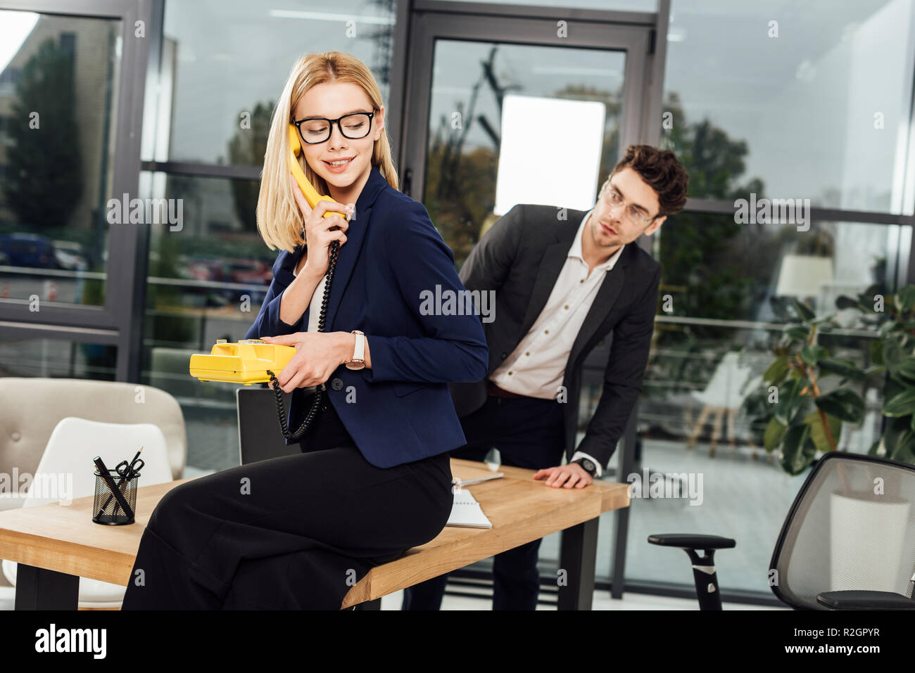 Imprenditore guardando il giovane imprenditrice con giallo telefono retrò a worklace in office Foto Stock