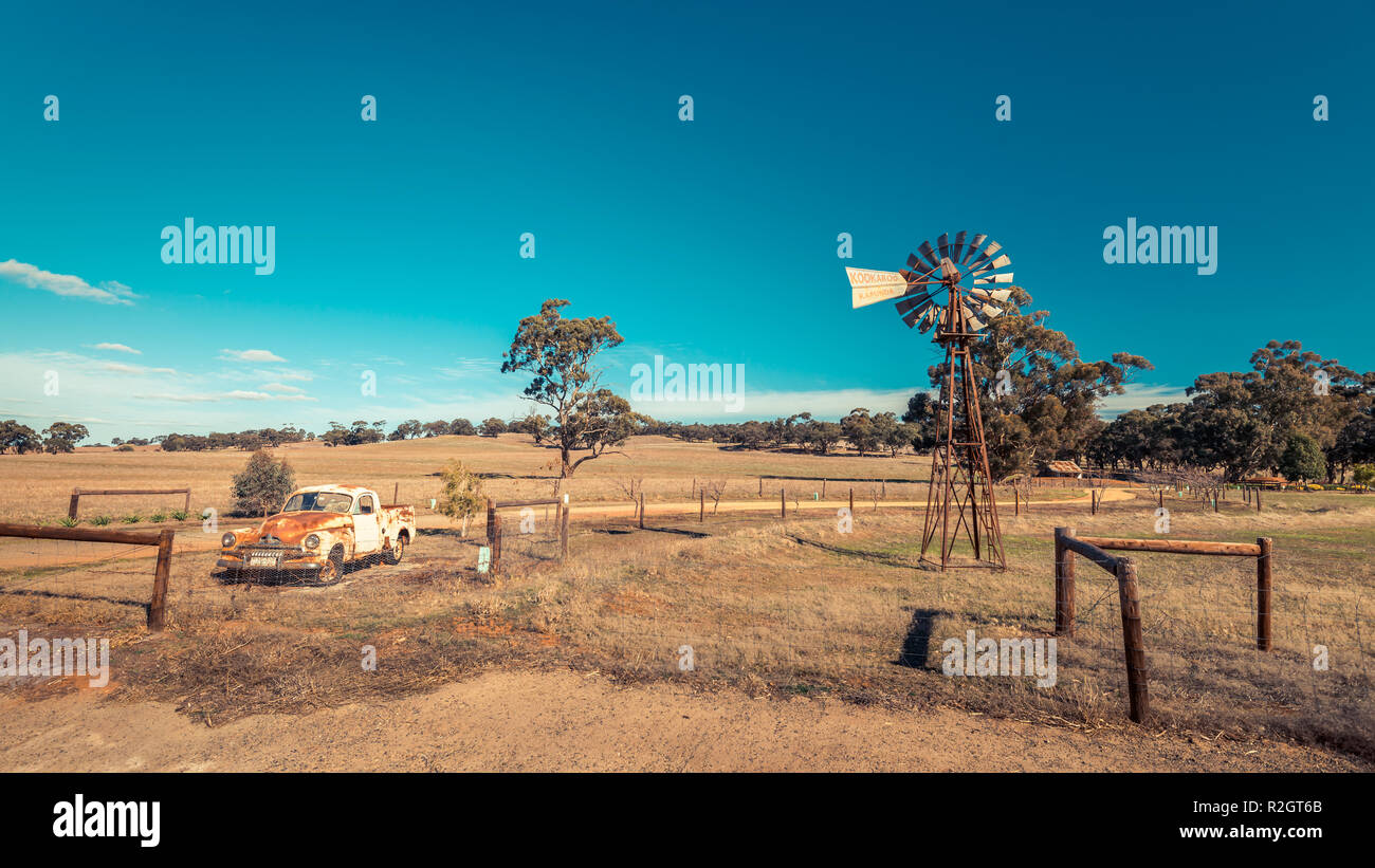 Kapunda, South Australia - Giugno 17, 2017: Rusty Holden FJ Ute e vintage Kookaroo mulino a vento sul display vicino a farm entrata dalla autostrada Foto Stock