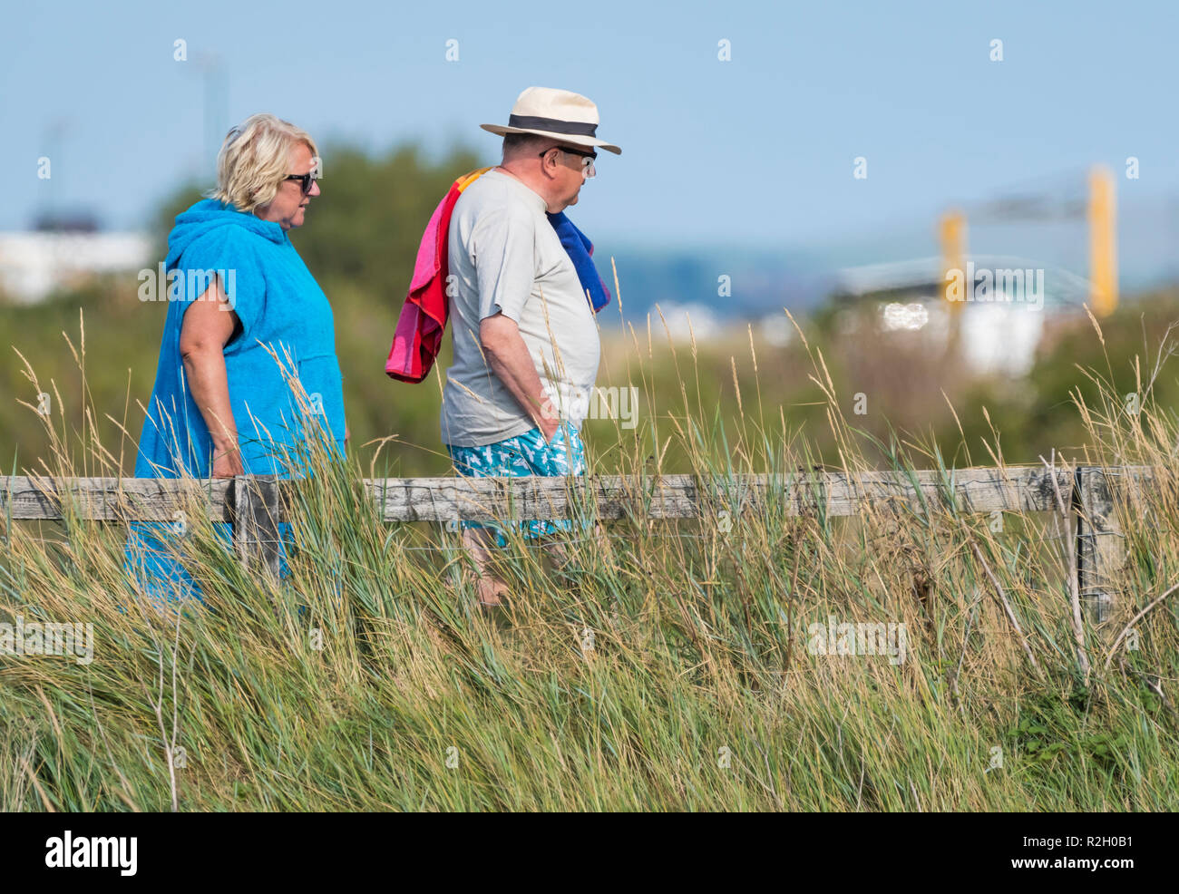 Vista laterale di un uomo di mezza età e la donna camminare portando un asciugamano in estate nel Regno Unito. Foto Stock