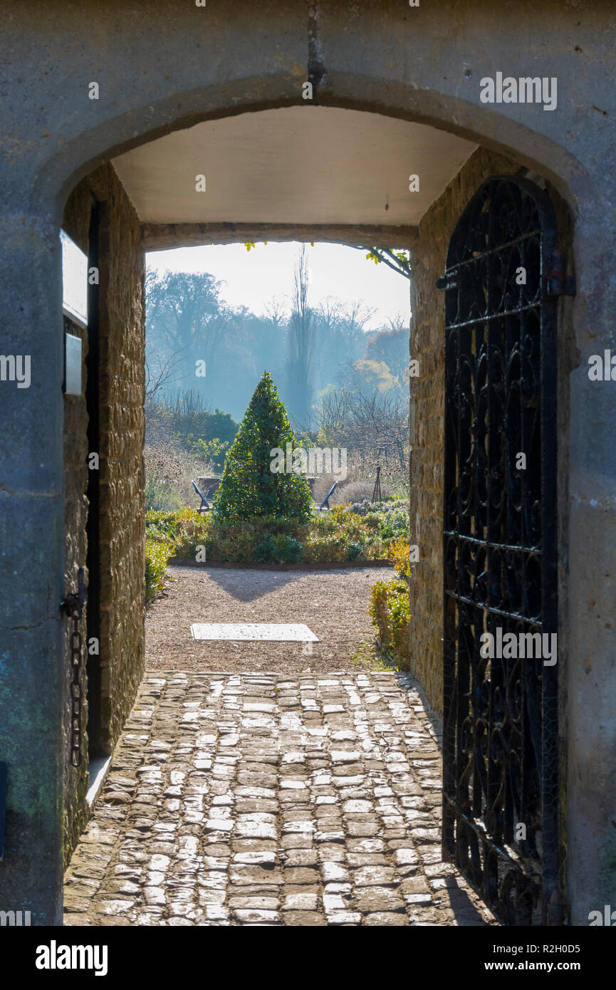 Passaggio stretto attraverso alcuni giardini con un cancello aperto nel Regno Unito. Il giardino segreto concetto. Foto Stock