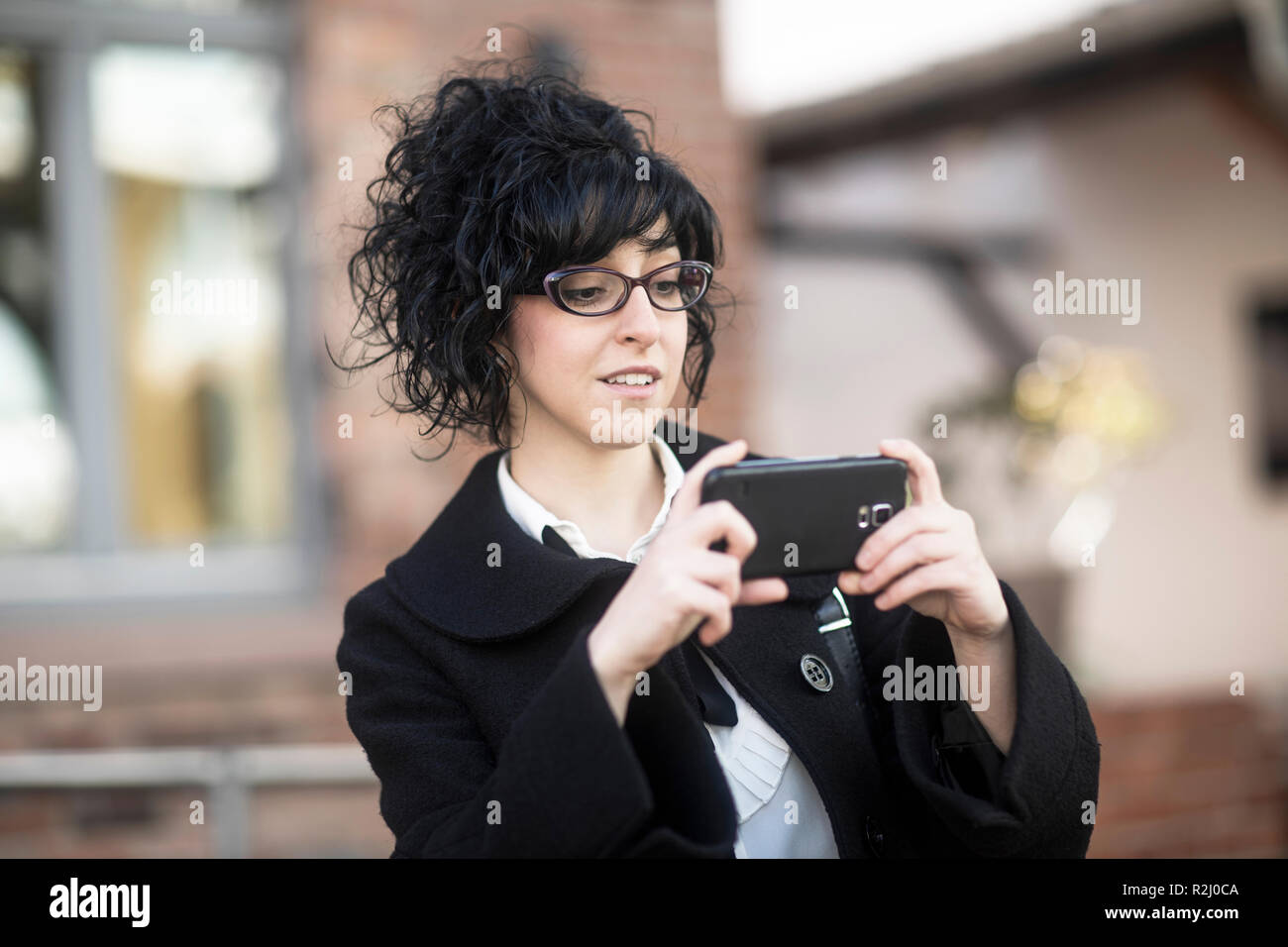 Donna sorridente in piedi all'esterno utilizzando il suo telefono cellulare, Germania Foto Stock