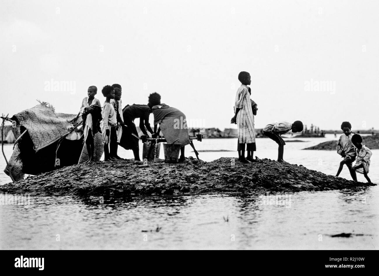 Sudan durante la carestia periodo di maggio-giugno 1985. Girba 2 Campo di Rifugiati. Questa immagine scansionata in 2018 bambini godersi l'acqua dopo dopo la pioggia caduta nella notte che ha provocato inondazioni e intorno al campo. Utilizzando acqua tubo Foto Stock