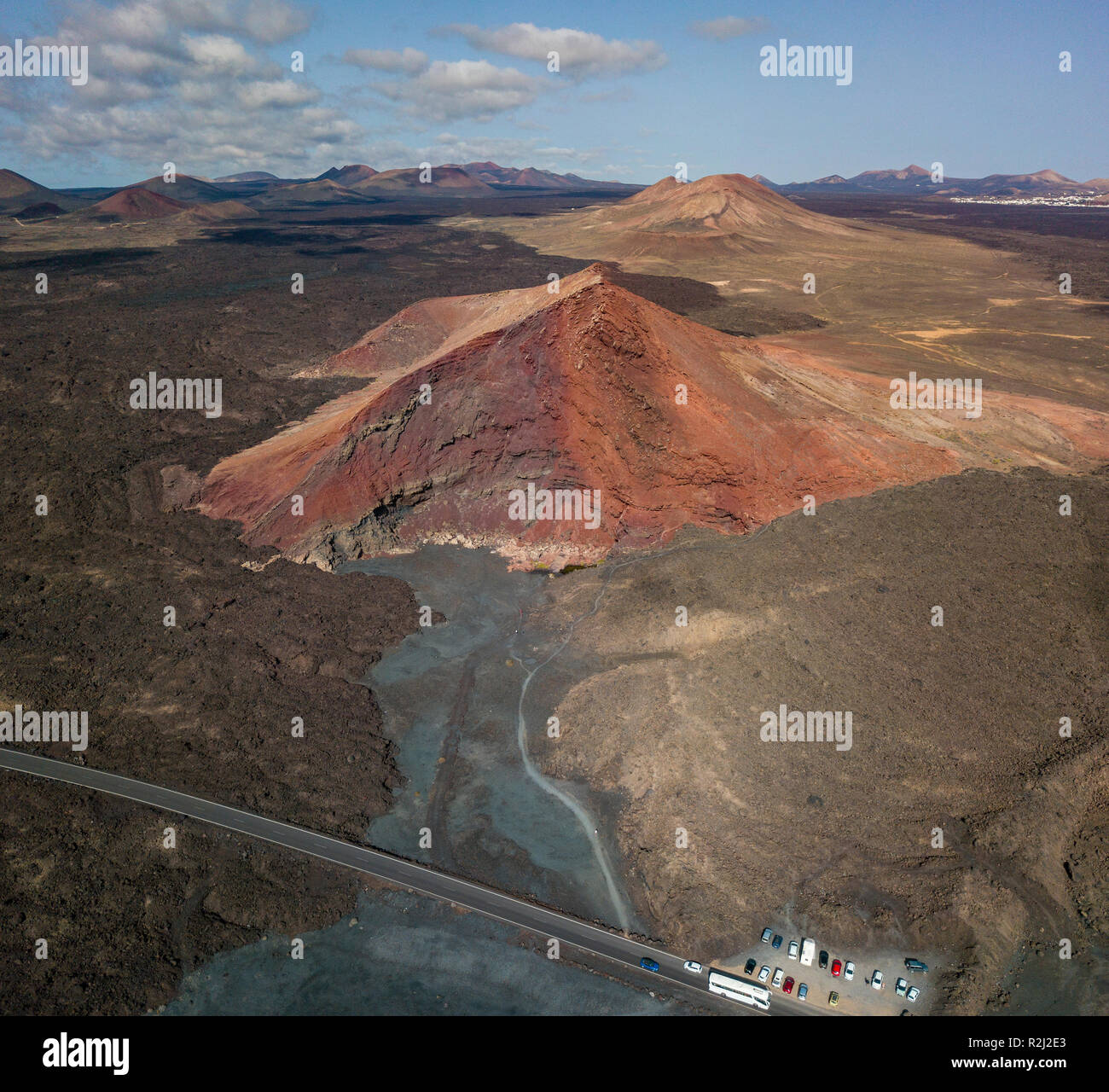 Vista aerea del Bermeja montagna di un colore rosso intenso, circondato da campi di lava. Strada costiera che fluisce attraverso il nero campo di lava. Lanzarote Spagna Foto Stock