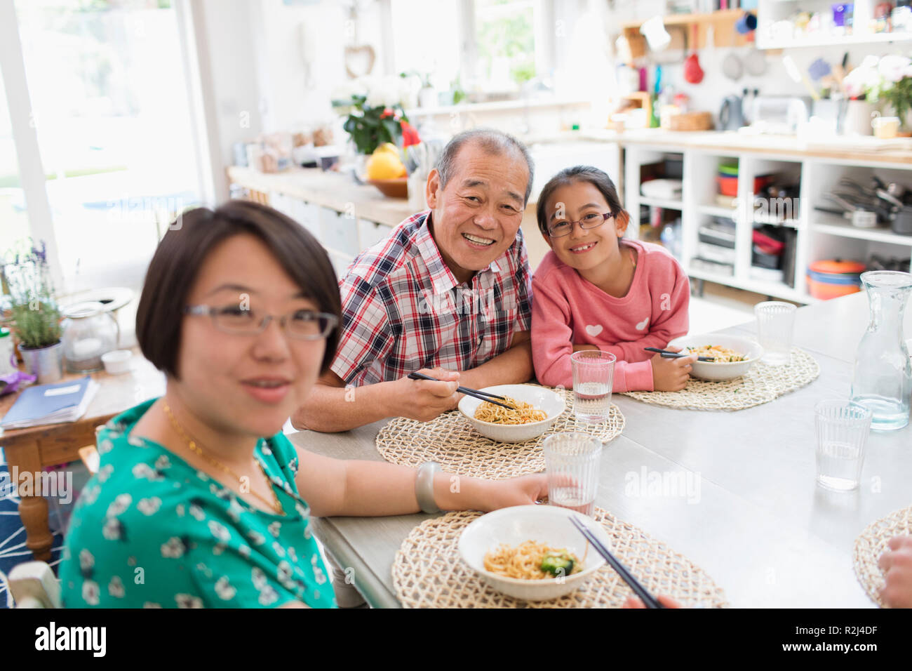 Ritratto felice multi-generazione famiglia mangiare tagliatelle con bacchette a tavola Foto Stock