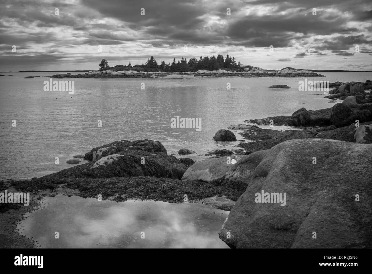 Una drammatica immagine in bianco e nero della costa rocciosa del Maine al tramonto con nuvole riflettono in un tidepool e un'isola a distanza. Foto Stock