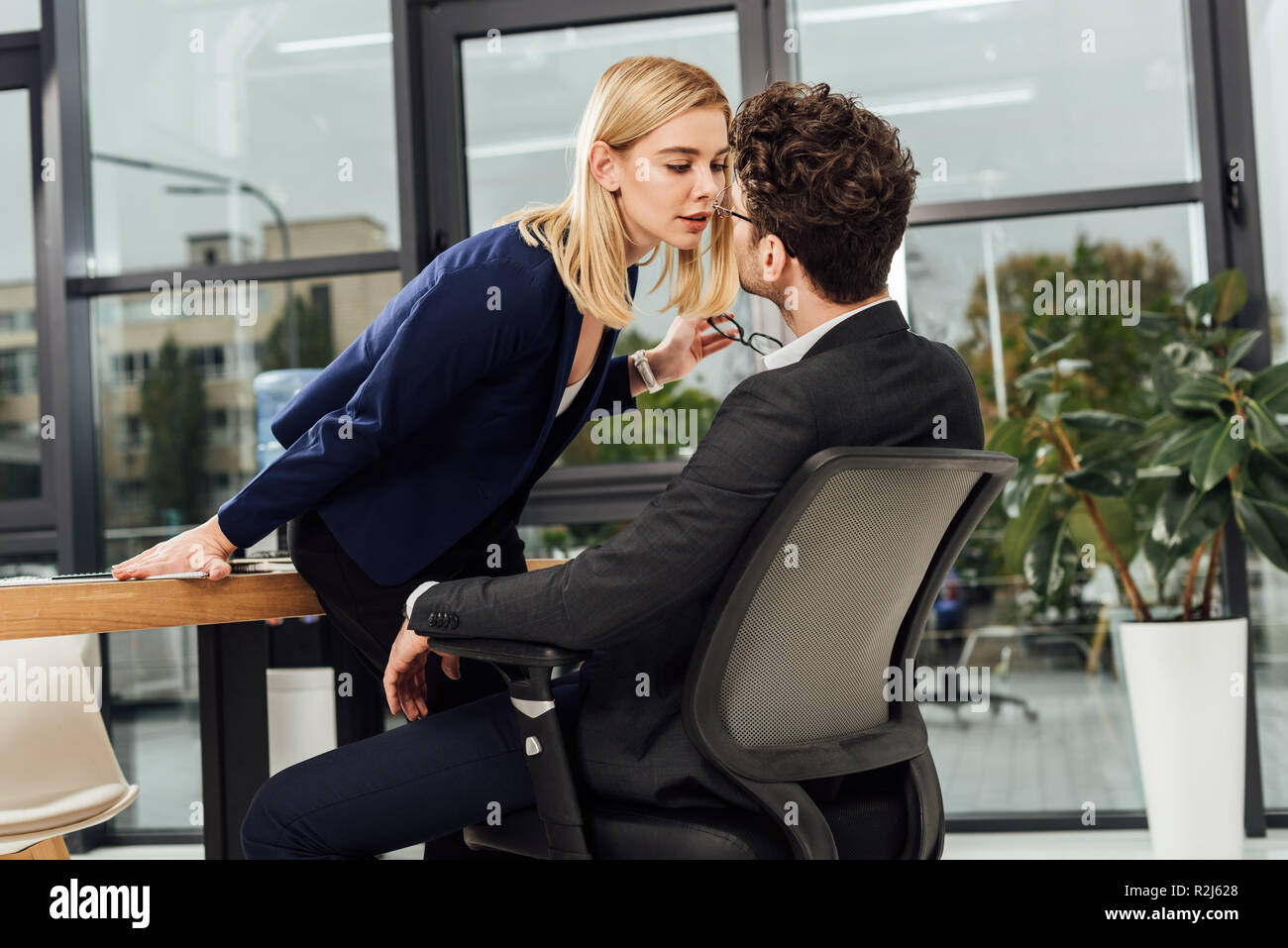 Vista laterale di attraenti imprenditrice flirtare con la collega di lavoro al lavoro in ufficio Foto Stock