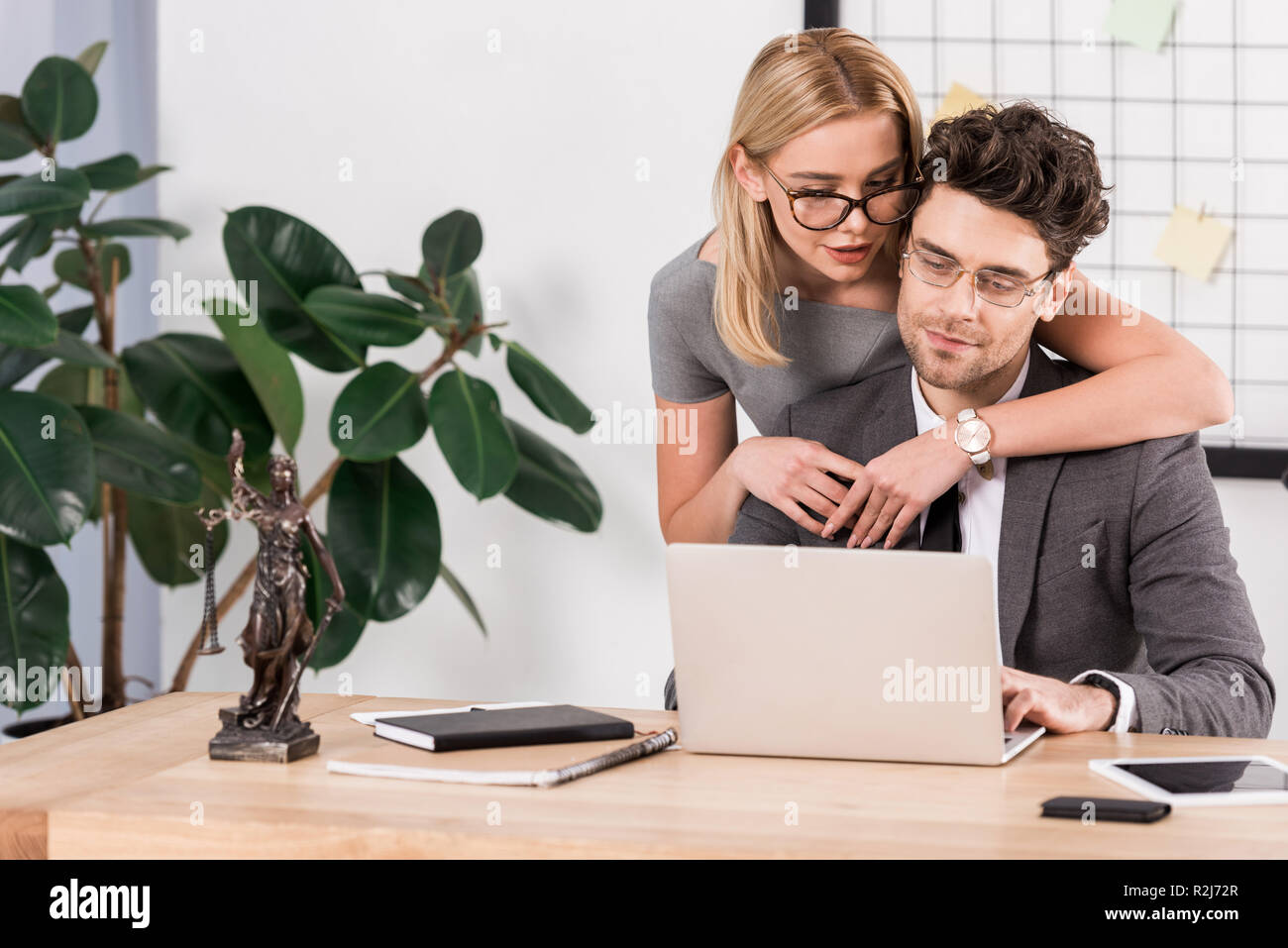 Ritratto di donna avvocato abbracciando un collega sul luogo di lavoro con computer portatile in ufficio, flirtare e ufficio concetto romantico Foto Stock