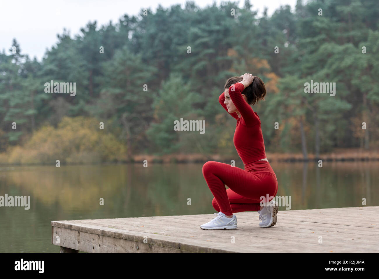 Donna vestita in abbigliamento sportivo di occupare i suoi capelli prima di eseguire al di fuori accanto a un lago Foto Stock