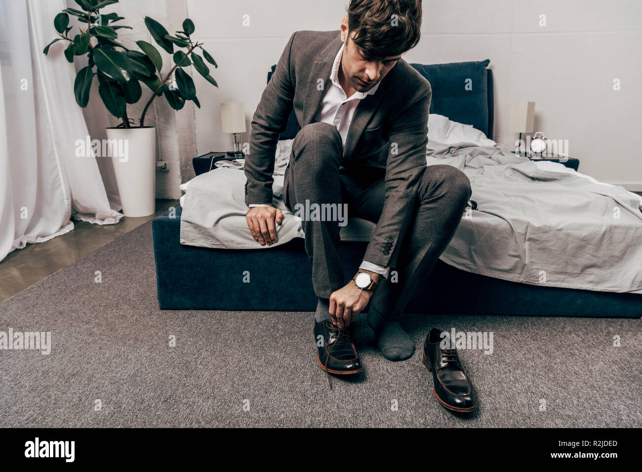 Imprenditore in abito formale mettendo su scarpe in camera da letto a casa Foto Stock