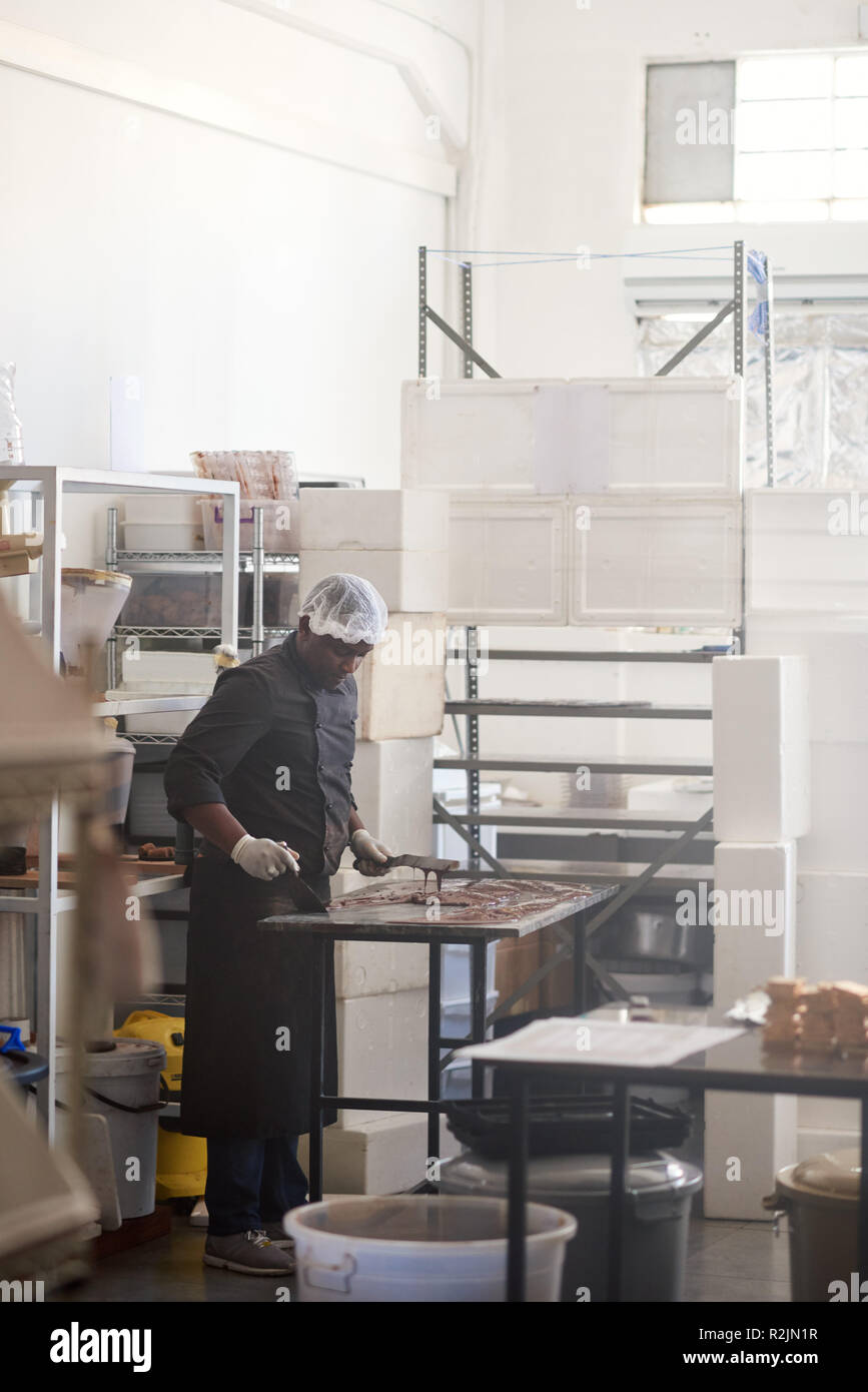 Lavoratore cioccolato spandimento su una confetteria rendendo tabella di fabbrica Foto Stock