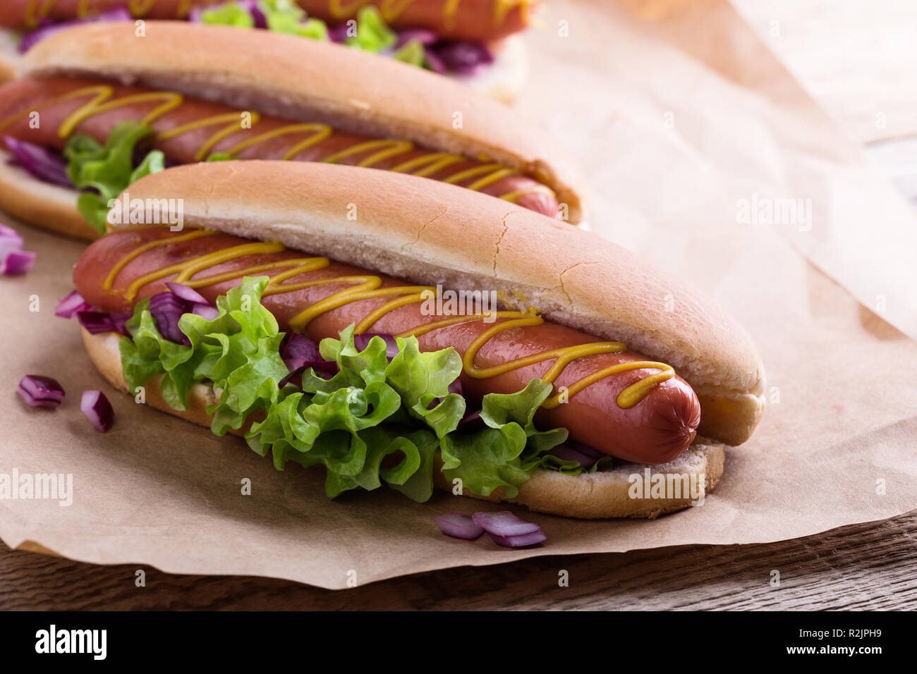 Hot Dog con giallo senape, lattuga e cipolle sulla carta craft, close up Foto Stock