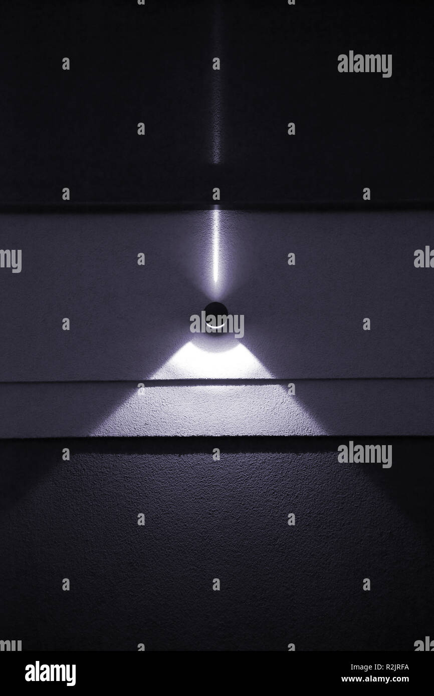 Close-up di radiatore da parete su una pianura parete in calcestruzzo che produce raggi di luce e coni di luce durante la notte. Foto Stock