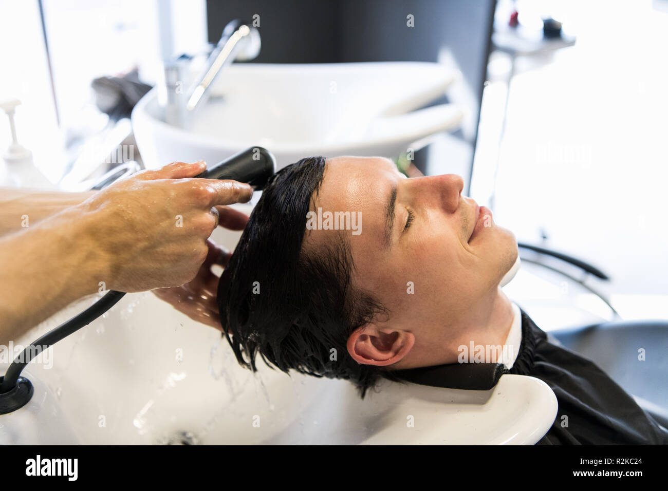 Uomo bello avente i suoi capelli lavati nel salone di parrucchiere. Giovane uomo disteso con gli occhi chiusi nel salone di bellezza. Foto Stock