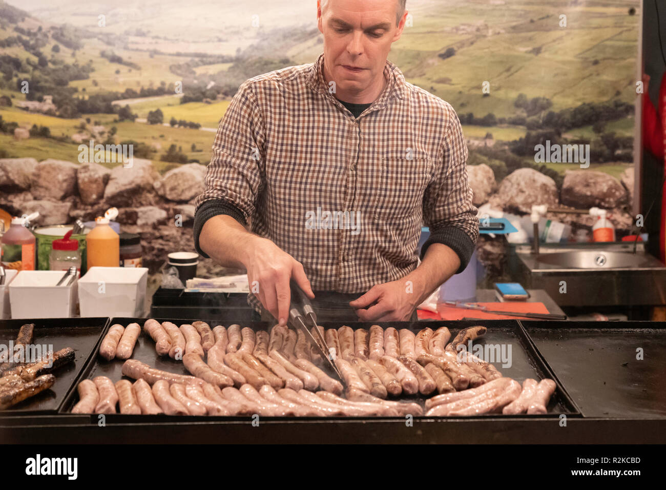 Uomo friggere un sacco di salsicce su una piastra commerciale in un mercatino di Natale all'aperto a Harrogate, North Yorkshire, Inghilterra, Regno Unito. Foto Stock
