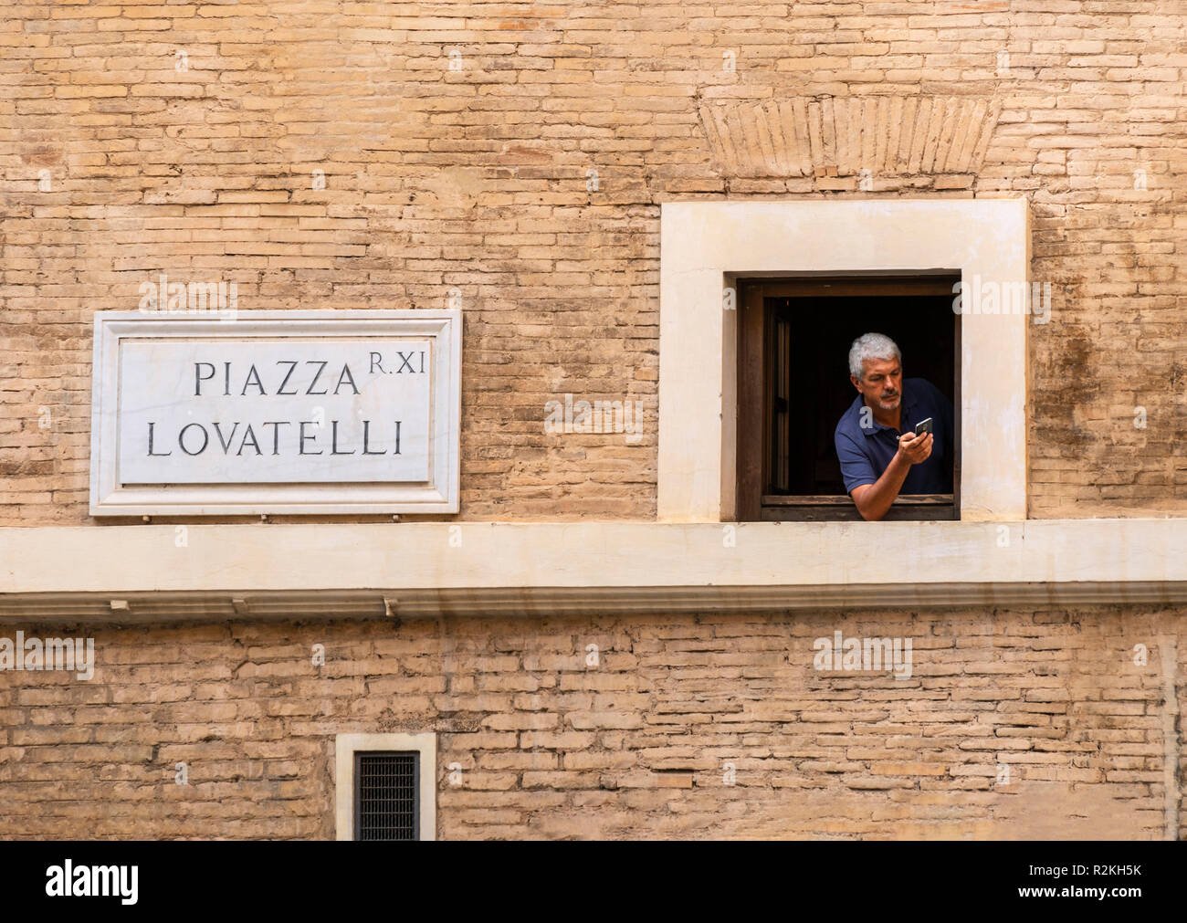 L'uomo cerca di segnale telefonico da una finestra in Piazza Lovatelli, rione XI - Sant'Angelo, Roma, Italia Foto Stock