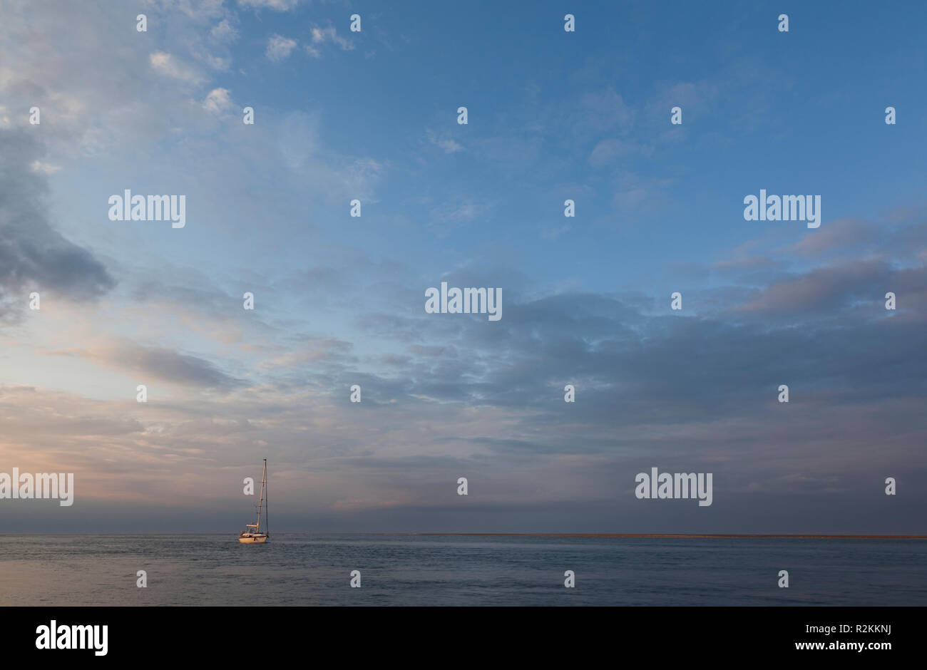 Una barca a vela su un mare calmo come il sole tramonta Foto Stock