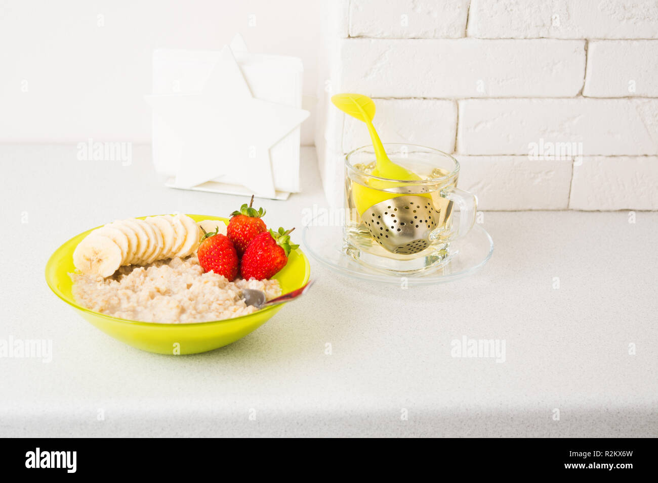 Farina di avena porridge con banana e fragola in verde ciotola con tè caldo e sana colazione su sfondo chiaro con spazio di copia Foto Stock