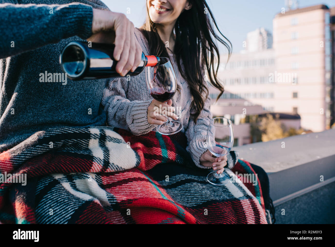 Ritagliato colpo di coppia giovane che copre in plaid sul tetto e busbana francese il vino rosso in bicchieri Foto Stock