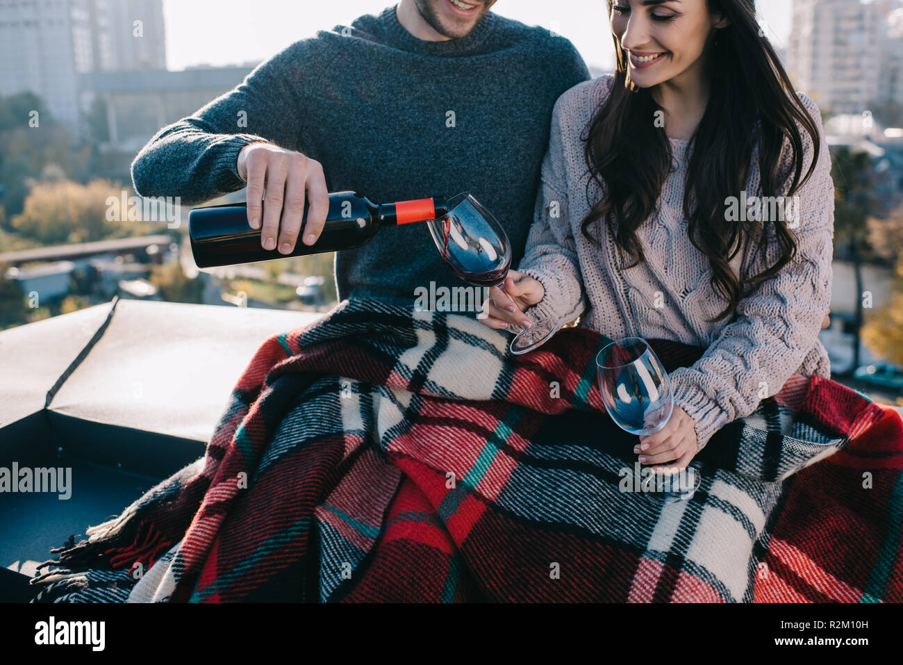 Ritagliato shot di felice coppia giovane che copre in plaid sul tetto e busbana francese il vino rosso in bicchieri Foto Stock