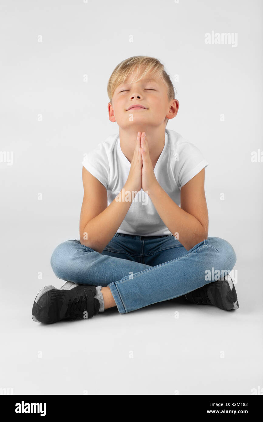 Età elementari biondo ragazzo che prega o che desiderano e sorrisi Foto Stock