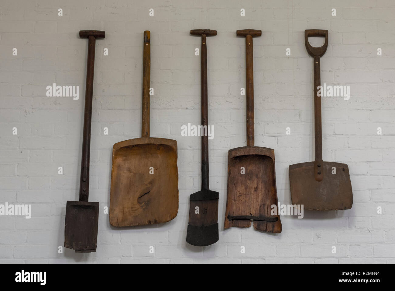 Una collezione di antichi o vintage malto pale e attrezzi agricoli appeso a una parete a casa holkham in Norfolk. Foto Stock