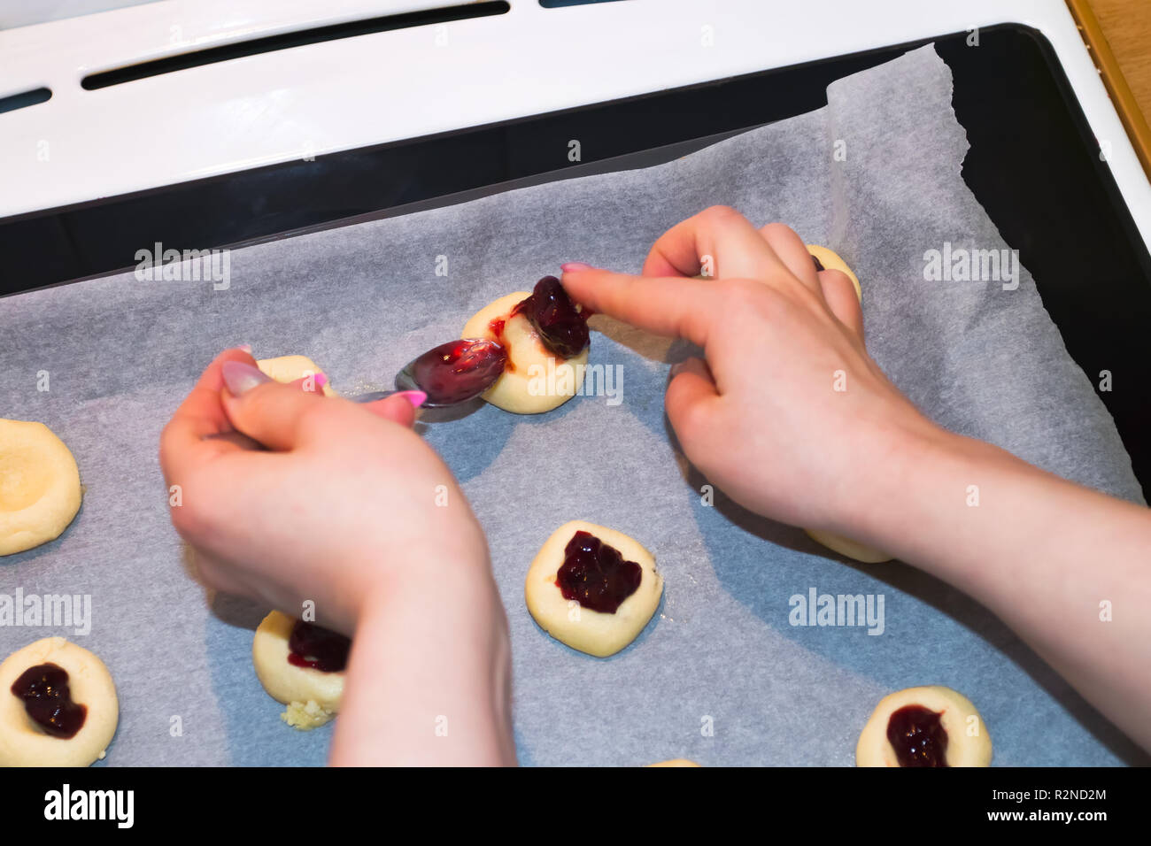 Giovane donna crudi di riempimento i biscotti con la marmellata gelatinosa. Baing in cucina domestica. Foto Stock