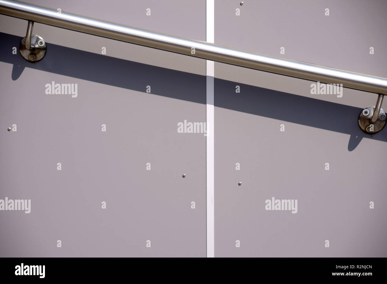 Maniglia in acciaio inox su un muro grigio con rivestimento in plastica getta un ombra, Foto Stock