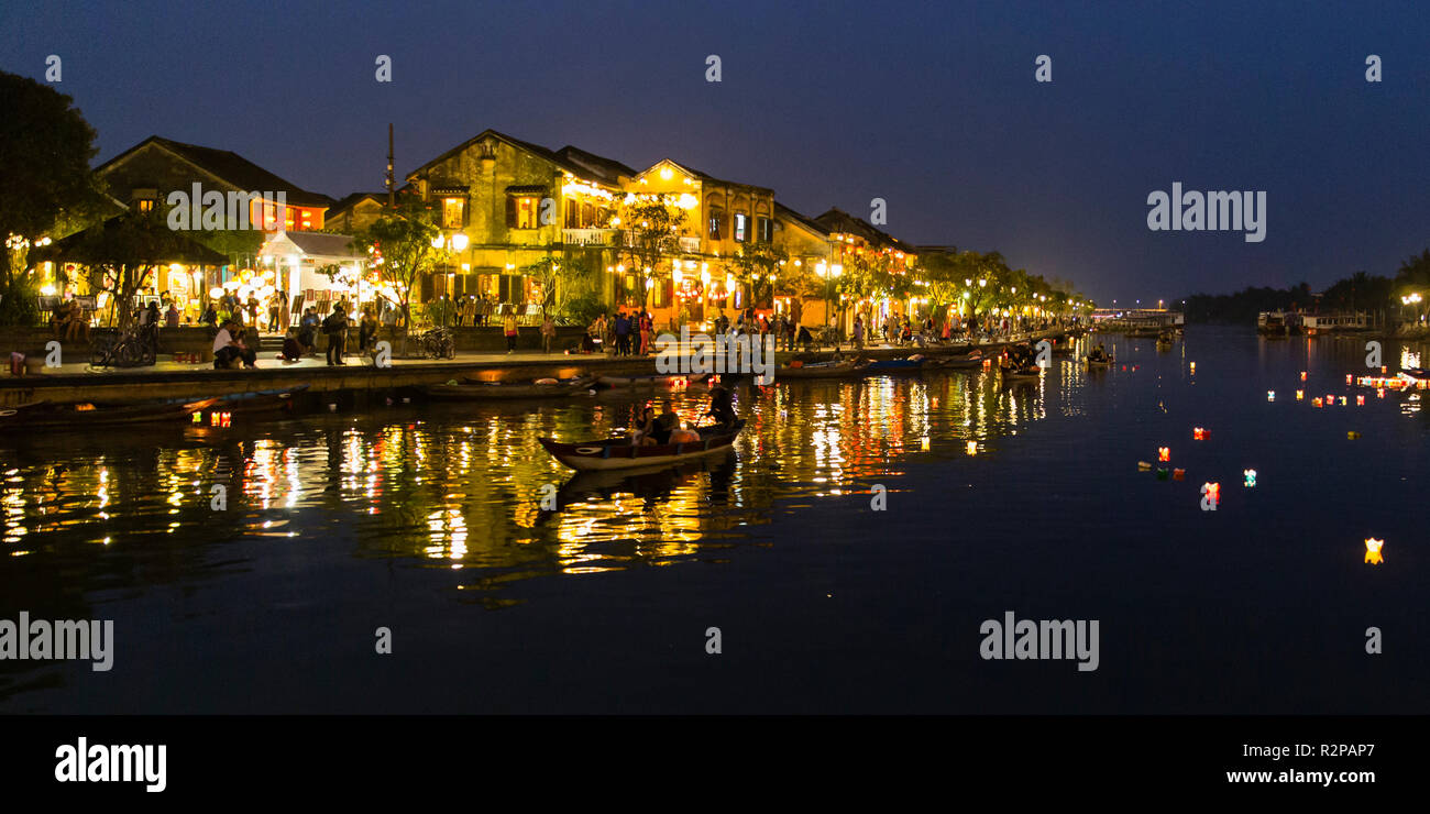 Illuminata, storico Hoi An Old Town di sera, preso dal ponte, riflessi di luci, barca e candele galleggianti sull'acqua, panorama Foto Stock