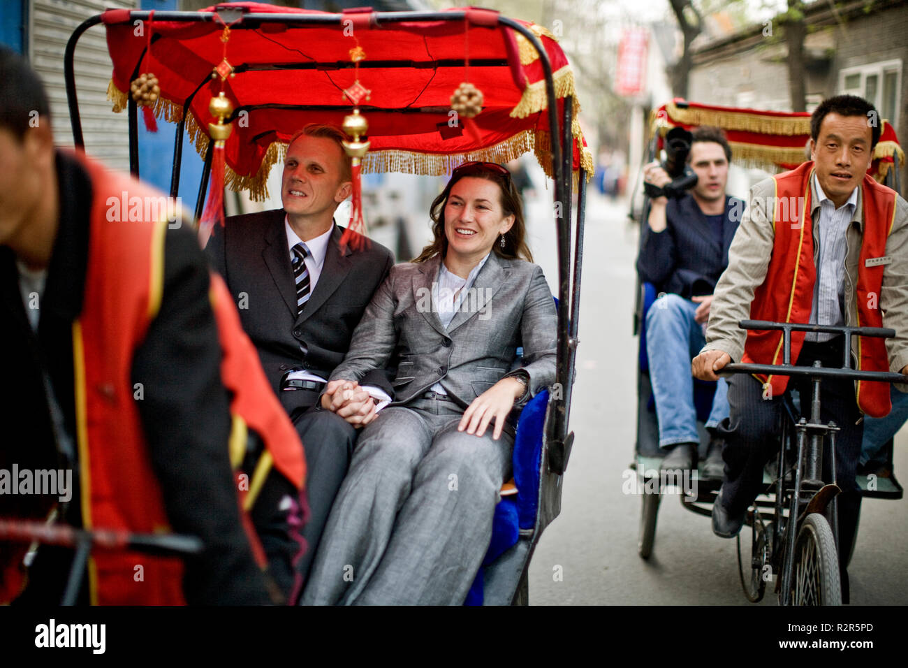 Turisti sorridente di equitazione in pedicabs lungo una strada di città. Foto Stock