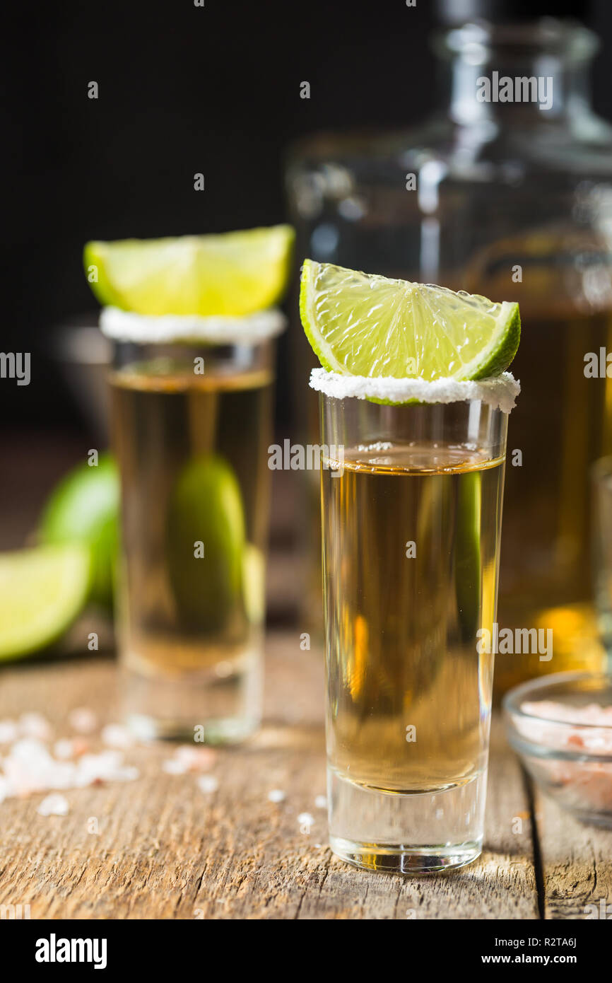 Mexican Gold Tequila riprese con calce e sale su un tavolo di legno su sfondo nero Foto Stock