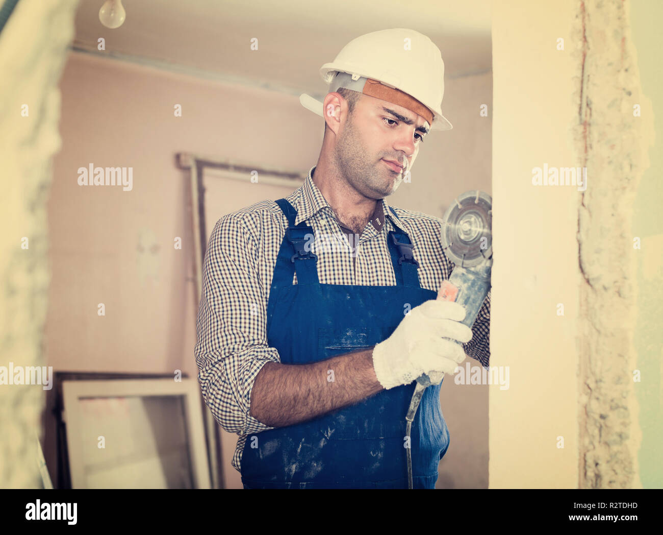 L uomo nel casco è segatura di parete con una sega circolare in mani. Foto Stock