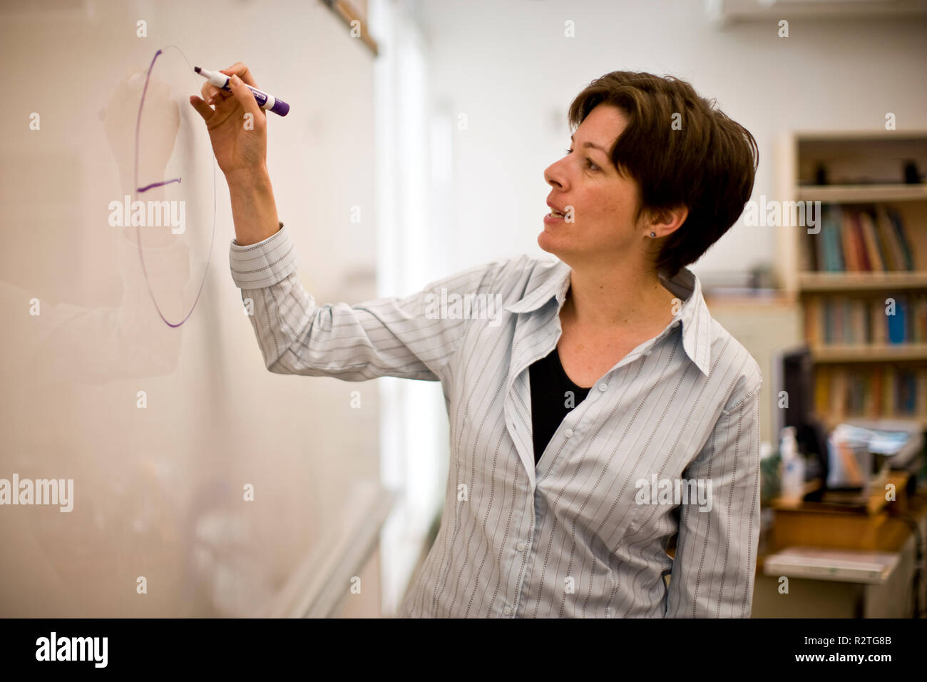 Metà femmina adulta insegnante scrivere sulla lavagna all'interno di una classe. Foto Stock