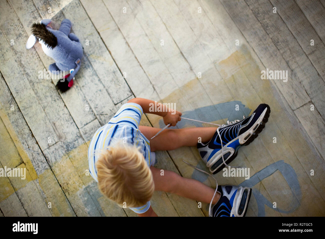 Bambino seduto sul pavimento con un giocattolo e mettendo sul suo padre's sneakers. Foto Stock