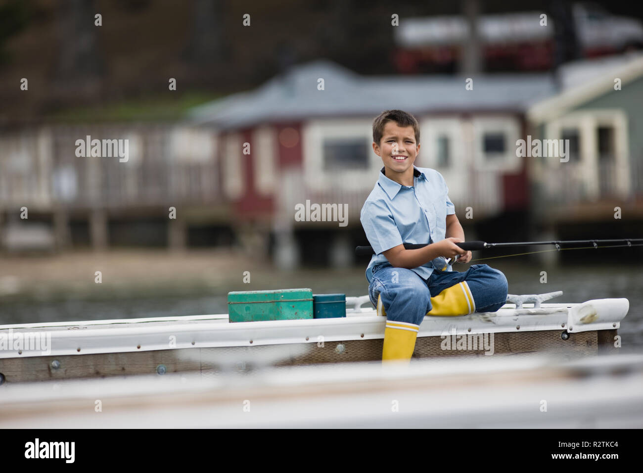 Ritratto di un sorridente ragazzo seduto mentre la pesca fuori dal bordo di un pontile. Foto Stock