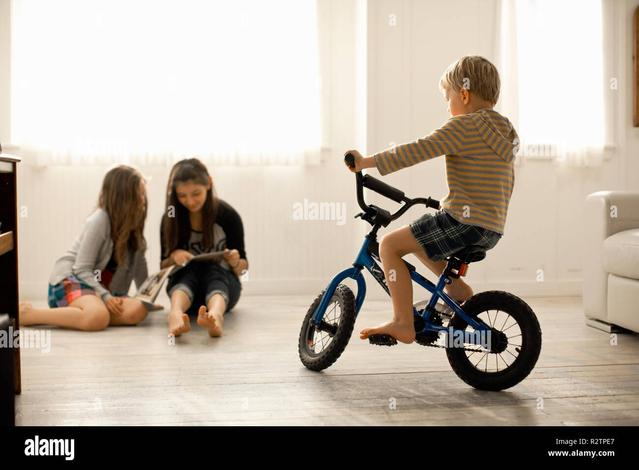 Due giovani ragazze seduti insieme su un pavimento a guardare un libro di ignorare un ragazzo su una bicicletta a guardarli. Foto Stock