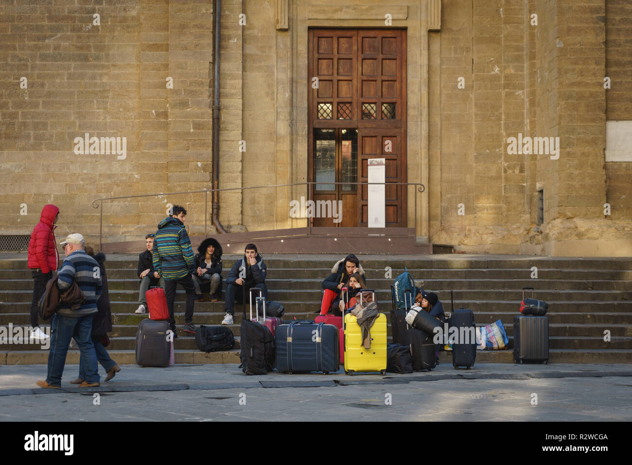 Firenze, Italia - Febbraio, 2019. Un gruppo di giovani turisti in gita scolastica seduti sui passi al di fuori della chiesa di San Lorenzo. Foto Stock