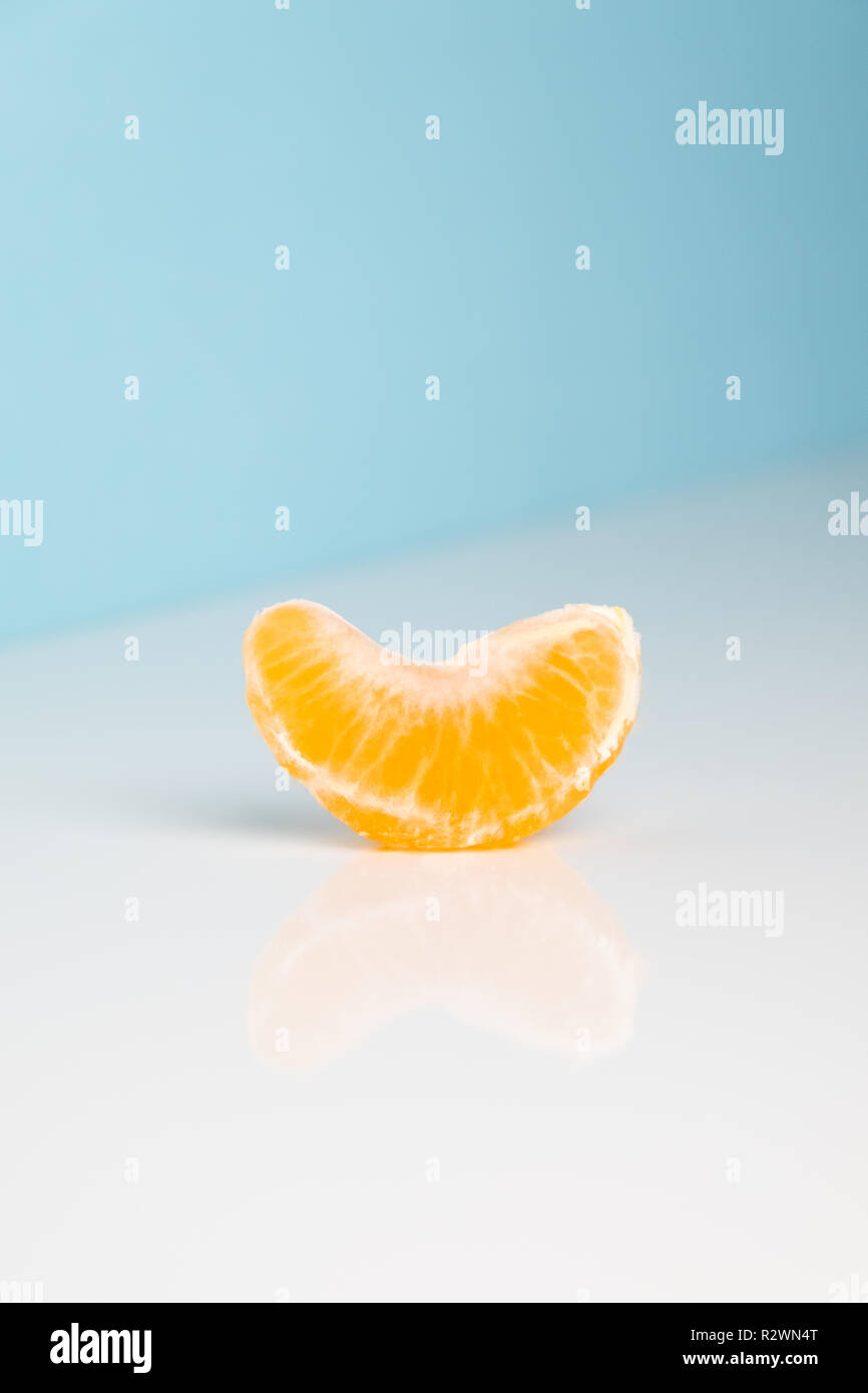 Il cuneo di mandarino su bianco e blu. Immagine minimalista del pezzo di frutta di arancia a sparse ambiente luminoso. Foto Stock