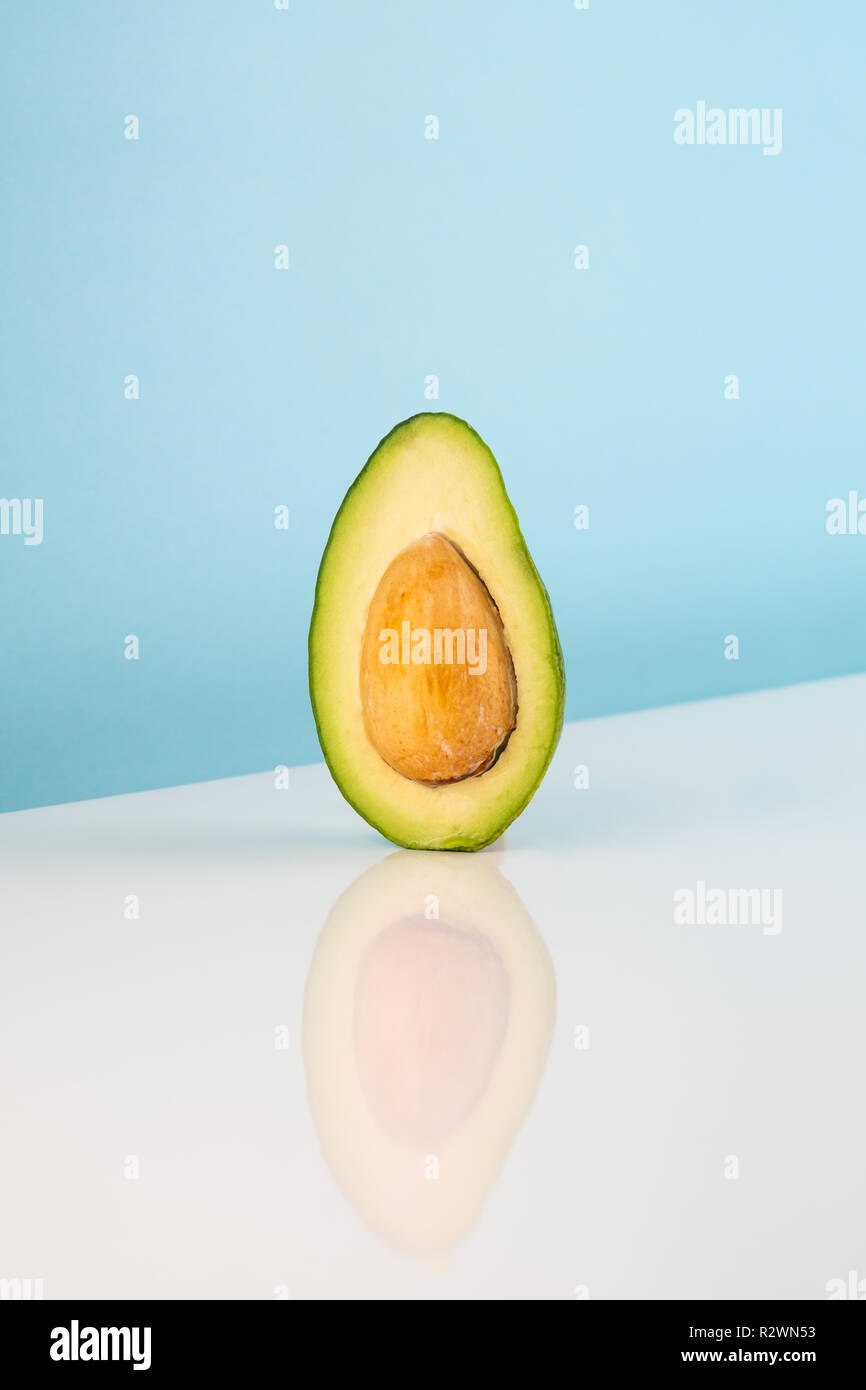 Metà frutto di Avocado sul tavolo bianco. Immagine minimalista del pezzo di Alligator Pear in studio luminoso sullo sfondo Foto Stock
