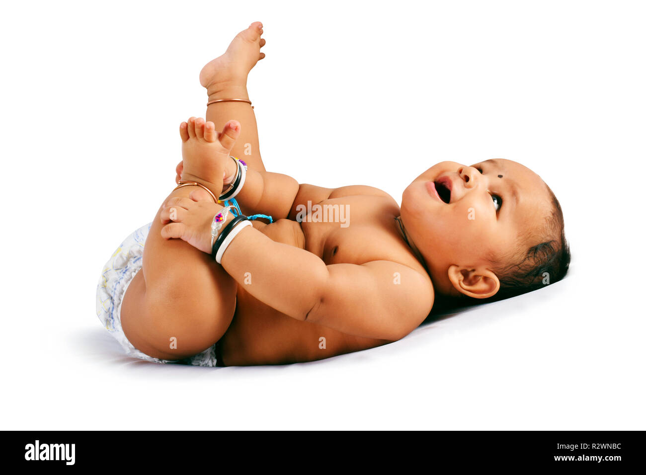 Carino il bambino dorme sul letto tenendo i piedi e ridere di Pune, Maharashtra. Foto Stock