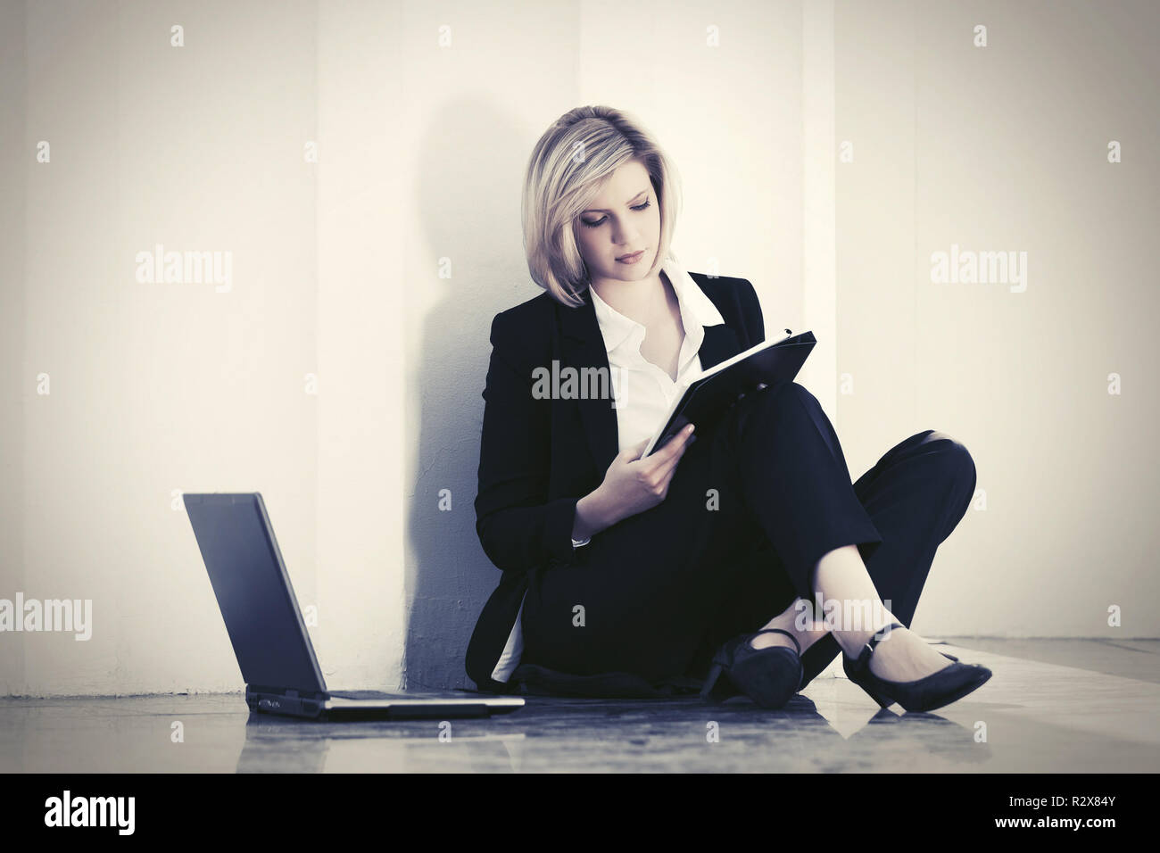 Giovane imprenditrice con laptop seduto alla parete elegante modello di moda in costume nero per esterno Foto Stock