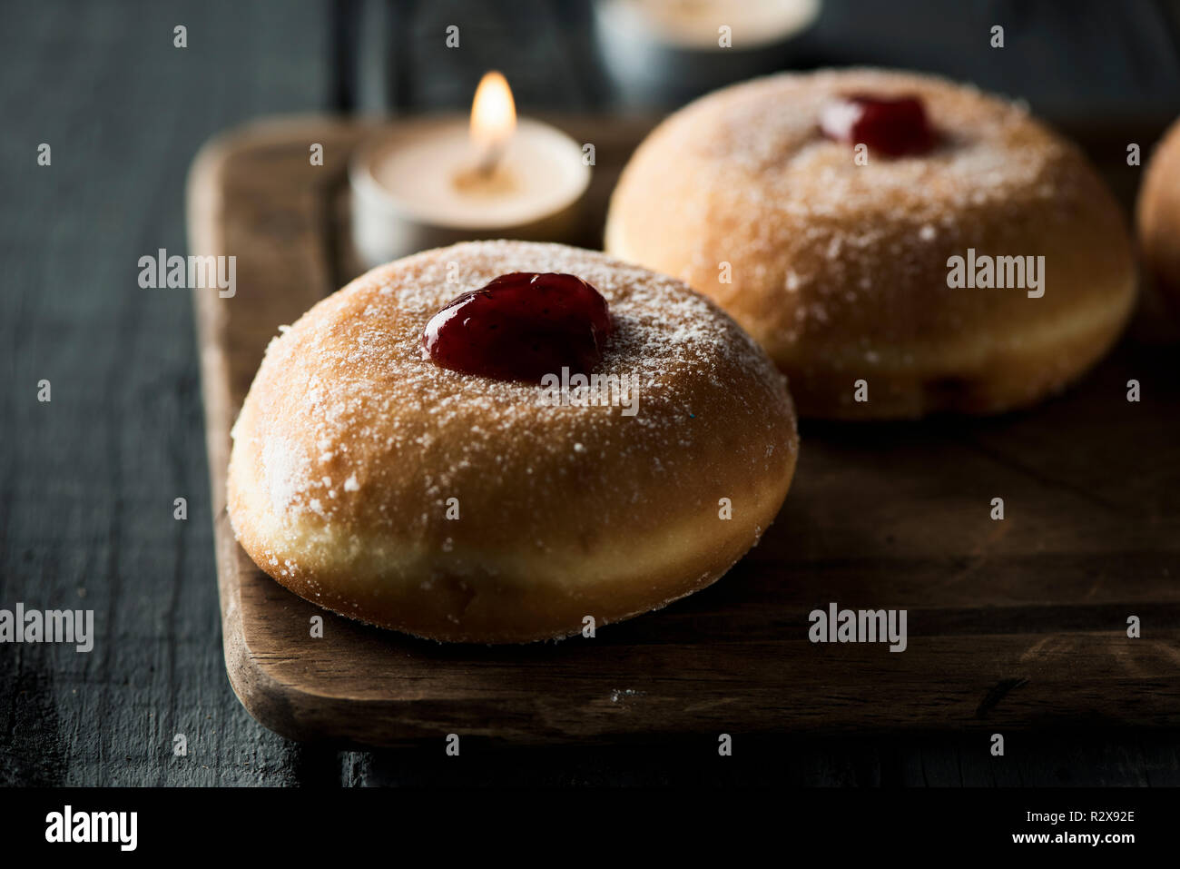 Primo piano di alcuni sufganiyot, ciambelle ebraica riempiti con marmellata di fragole tradizionalmente consumati su Hanukkah, e alcune candele accese, su una tavola in legno rustico Foto Stock