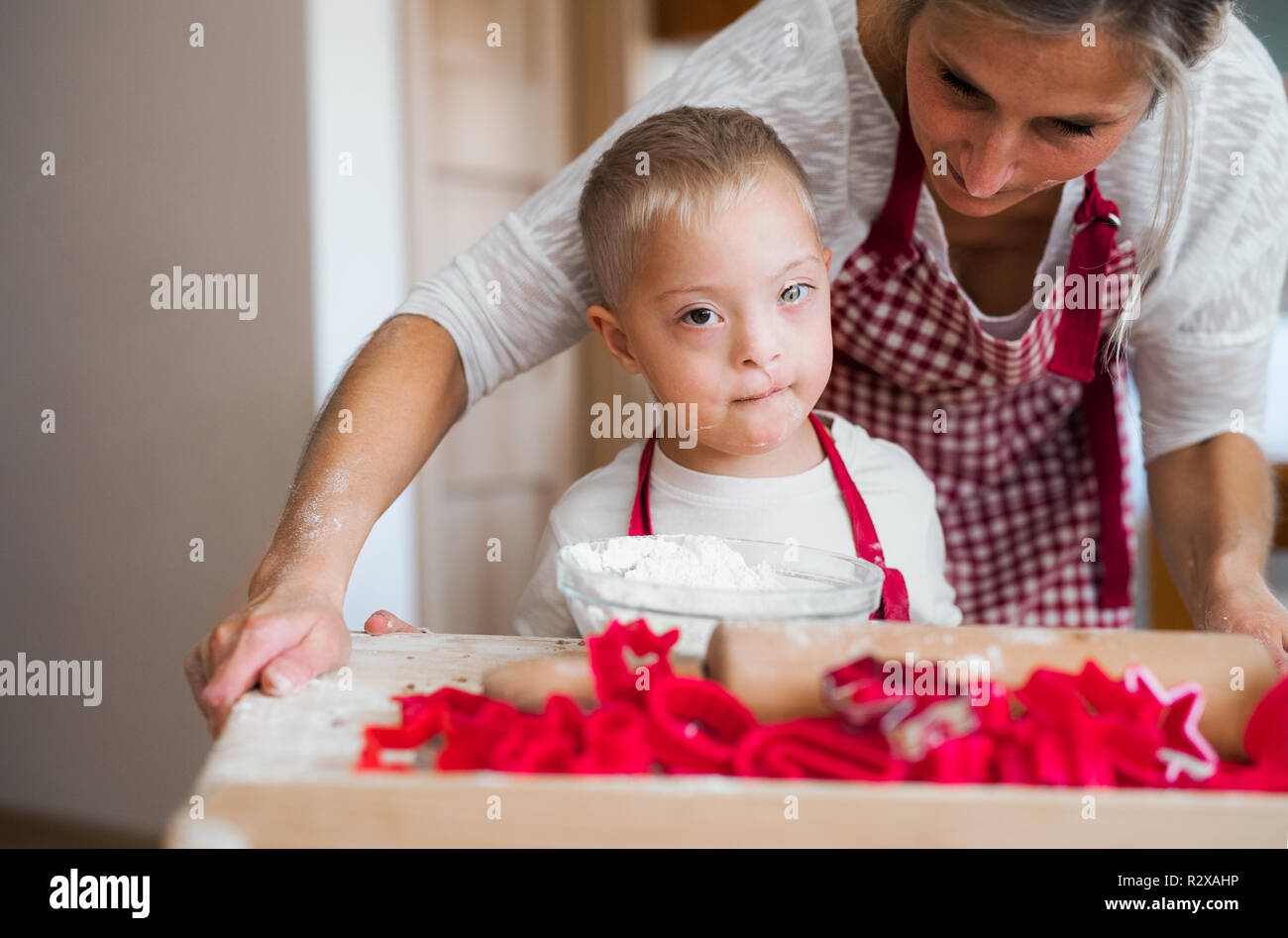 Un felice disabili affetti da sindrome di down bambino con sua madre in interni cottura. Foto Stock