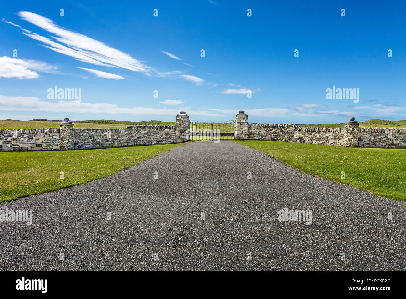 Strada che conduce verso il cancello chiuso nel muro di pietra con cielo blu, North Uist, Ebridi Esterne, Scotland, Regno Unito, Europa Foto Stock