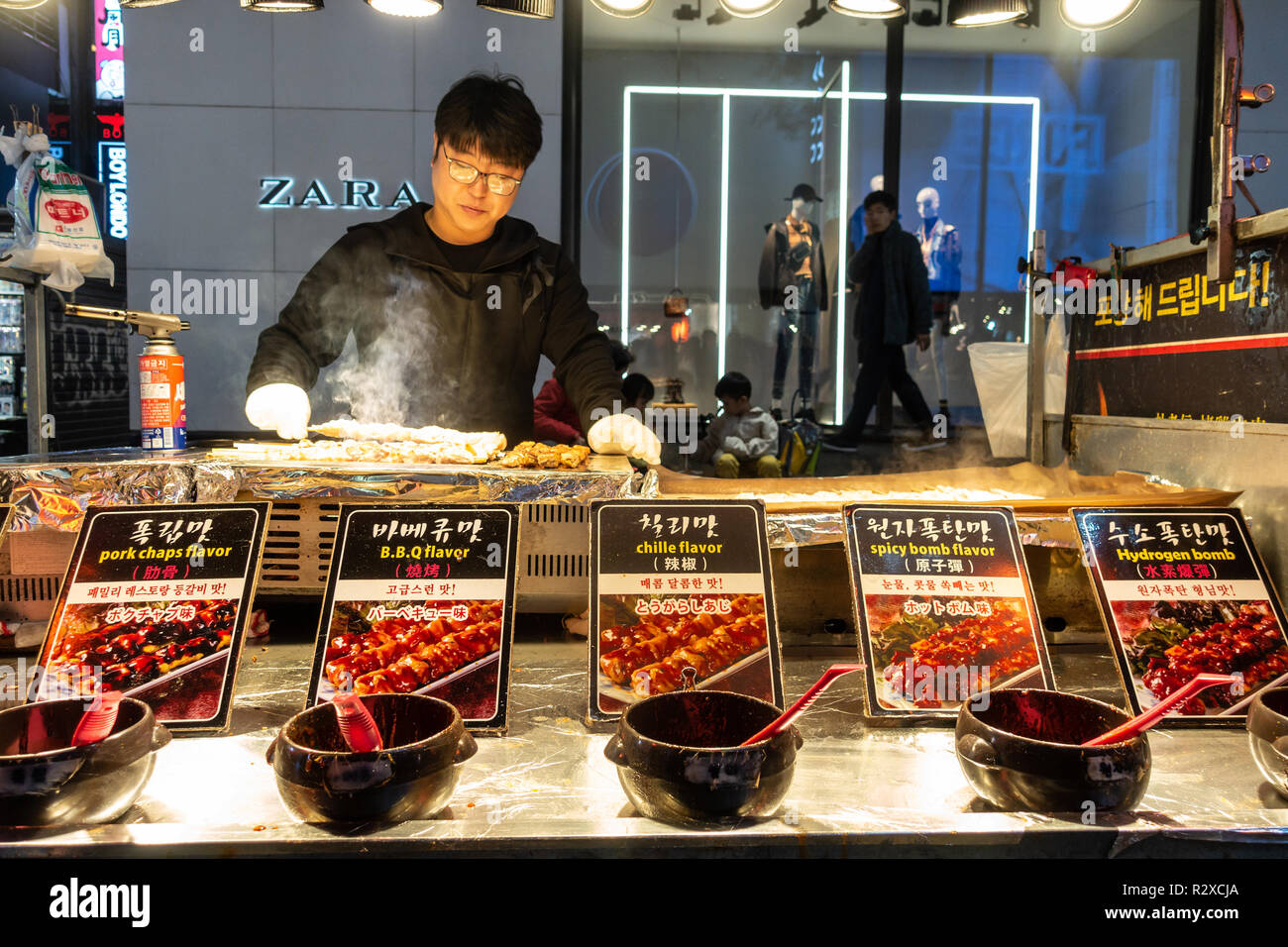 Un cibo di strada cuochi stallholder carne di maiale alla griglia spiedini sul suo in stallo a Myeongdong a Seul, Corea del Sud Foto Stock